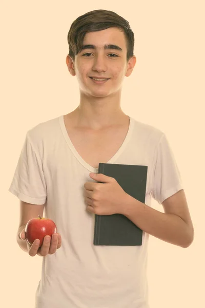 Estúdio tiro de jovem feliz adolescente persa sorrindo enquanto segurando livro e maçã vermelha — Fotografia de Stock