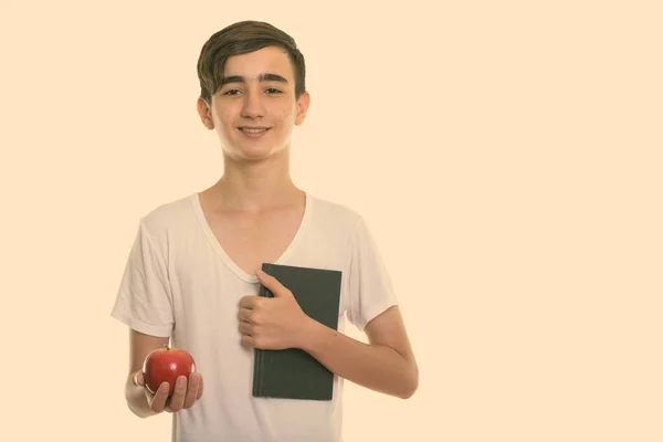 工作室拍摄的年轻快乐的波斯少年微笑着拿着书和红苹果 — 图库照片
