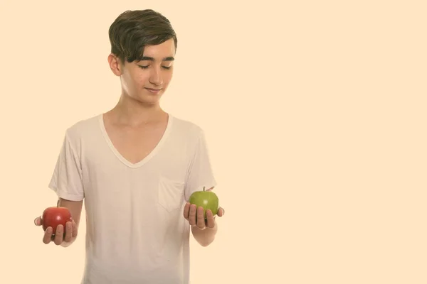 Studio shot van jonge knappe Perzische tiener jongen met rode appel en kijken naar groene appel — Stockfoto