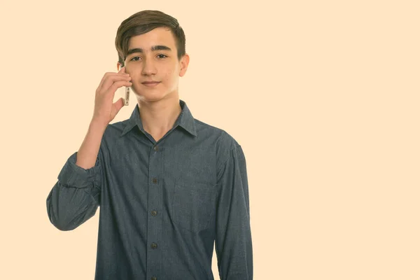 Studio shot of young handsome Persian teenage boy talking on mobile phone — Stock Photo, Image