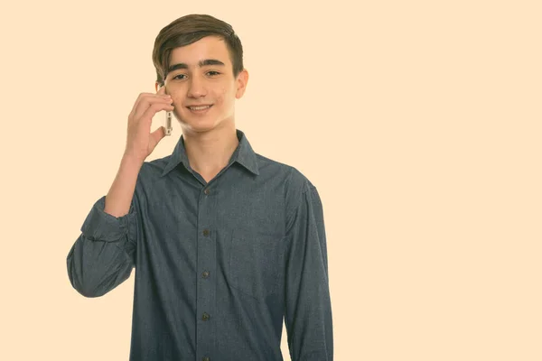 Studio shot of young happy Persian adolescent garçon souriant tout en parlant sur téléphone mobile — Photo