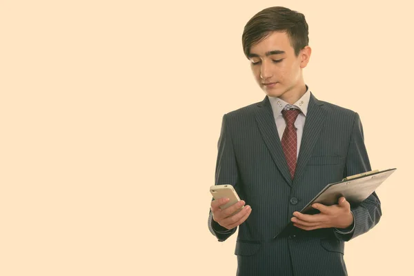 Estúdio tiro de jovem bonito adolescente empresário persa usando telefone celular enquanto segurando prancheta — Fotografia de Stock