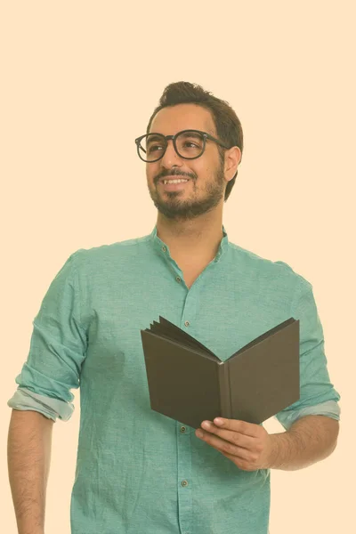 Jovem homem indiano feliz segurando livro enquanto pensa — Fotografia de Stock