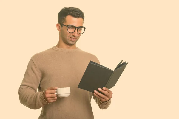 Jong gelukkig Iraanse man die boek leest terwijl hij koffiebeker vasthoudt — Stockfoto