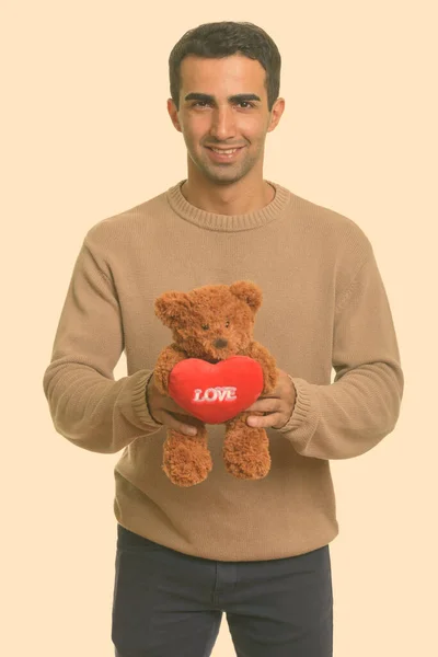 Молодой счастливый иранский мужчина держит плюшевого мишку с сердцем и знак любви готов к Дню Святого Валентина — стоковое фото