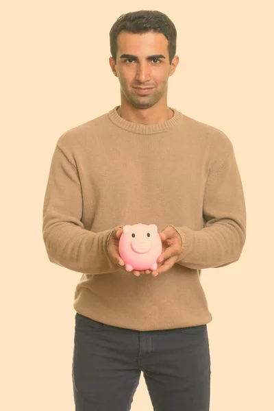 Young handsome Iranian man holding piggy bank — Stock Photo, Image