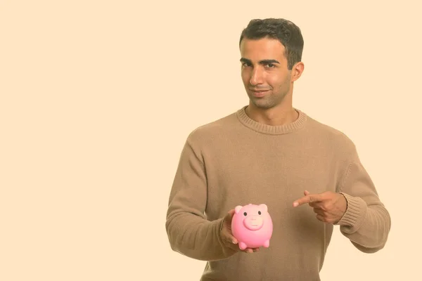 Young handsome Iranian man holding piggy bank and pointing finger — Stock Photo, Image