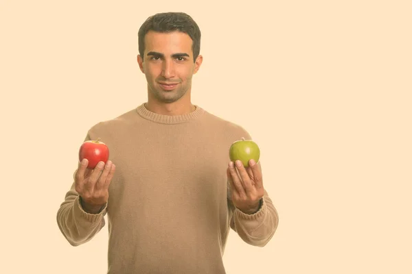 Joven hombre iraní guapo sosteniendo manzana roja y verde — Foto de Stock