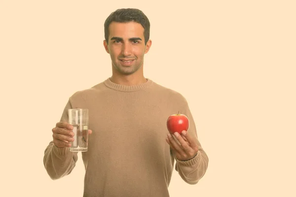Joven feliz hombre iraní sosteniendo manzana roja y vaso de agua — Foto de Stock