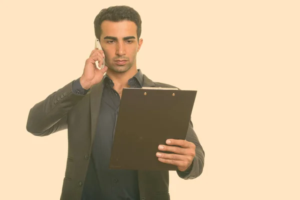 Young handsome Iranian businessman talking on mobile phone while reading clipboard