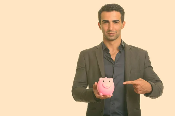 Young handsome Iranian businessman holding piggy bank while pointing finger — Stock Photo, Image