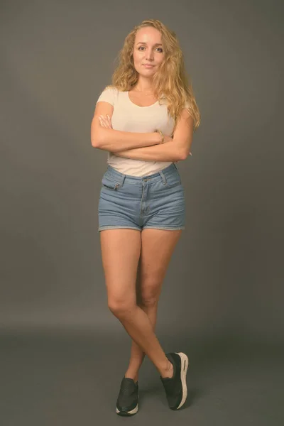 Junge schöne Frau mit langen welligen blonden Haaren vor grauem Hintergrund — Stockfoto