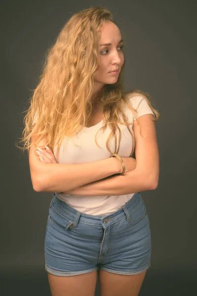 Jeune belle femme avec de longs cheveux blonds ondulés sur fond gris — Photo