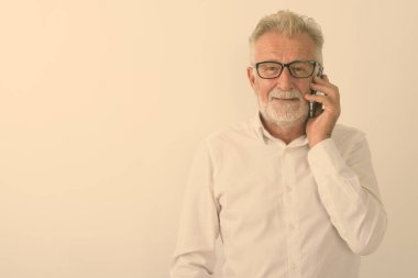 Cep telefonuyla konuşurken gülümseyen yaşlı ve sakallı bir adamın beyaz arka planda gözlüklü mutlu bir fotoğrafı.