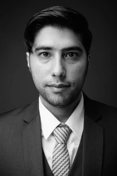 Studio shot of young handsome Iranian businessman against brown background