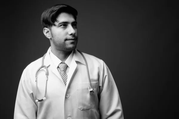 Studio shot of young handsome Iranian man doctor against brown background