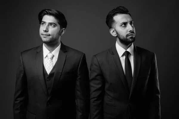 Studio shot of two young Iranian businessmen together against brown background