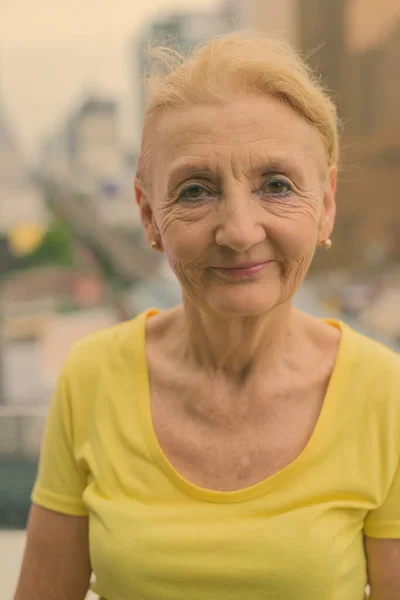 Vacker senior kvinna med blont hår mot utsikt över staden — Stockfoto