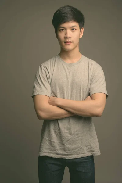 Young handsome Asian man against gray background — Stock Photo, Image