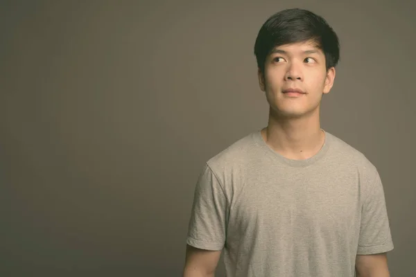 Genç yakışıklı Asyalı adam gri arka planda — Stok fotoğraf