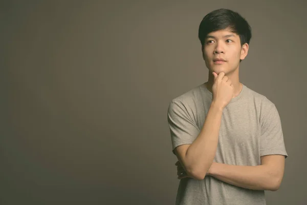 Genç yakışıklı Asyalı adam gri arka planda — Stok fotoğraf