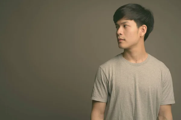 Joven guapo asiático hombre contra gris fondo —  Fotos de Stock