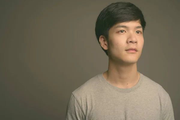 Young handsome Asian man against gray background — Stock Photo, Image