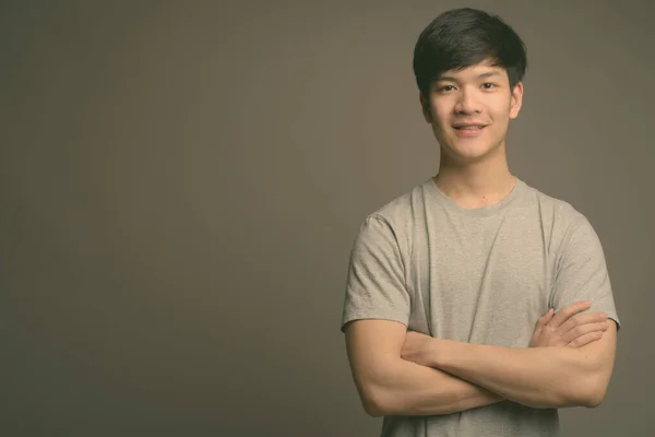 Joven guapo asiático hombre contra gris fondo — Foto de Stock