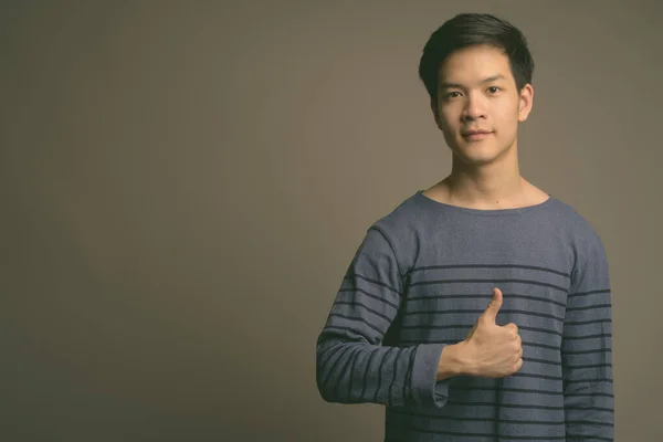 Young handsome Asian man against gray background — Stock Photo, Image