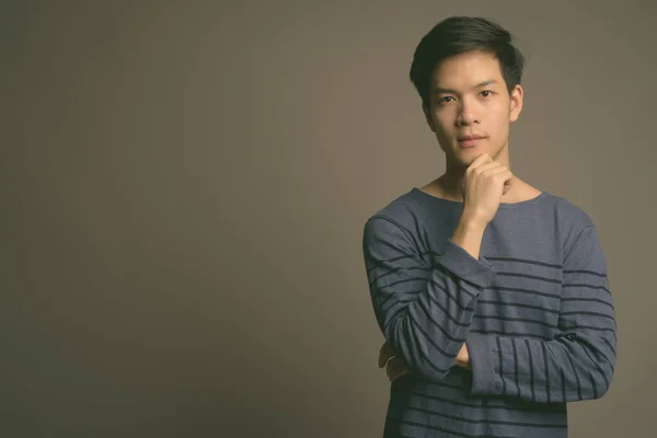 Young handsome Asian man against gray background — Stock Photo, Image