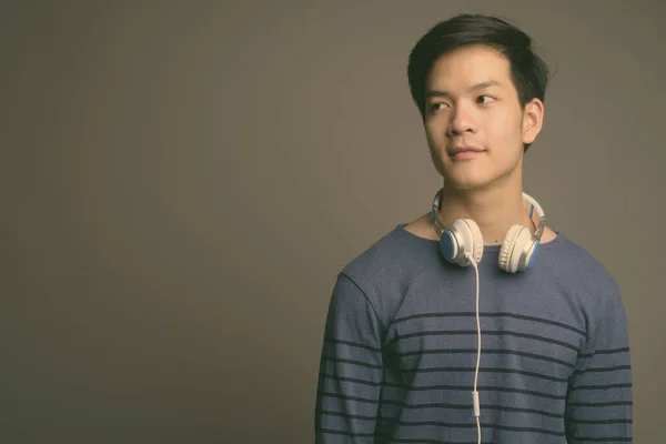 Молодий привабливий азіатський чоловік у навушниках на сірому фоні. — стокове фото