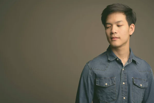 Молодий привабливий азіатський чоловік одягнений у джинсову сорочку на сірому фоні. — стокове фото