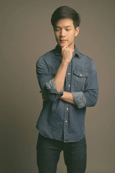 Young handsome Asian man wearing denim shirt against gray background — Stock Photo, Image