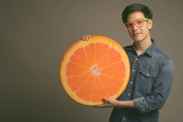 Joven guapo asiático hombre sosteniendo naranja almohada sobre gris fondo —  Fotos de Stock