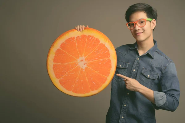 Giovane bello asiatico uomo holding arancio cuscino contro grigio sfondo — Foto Stock