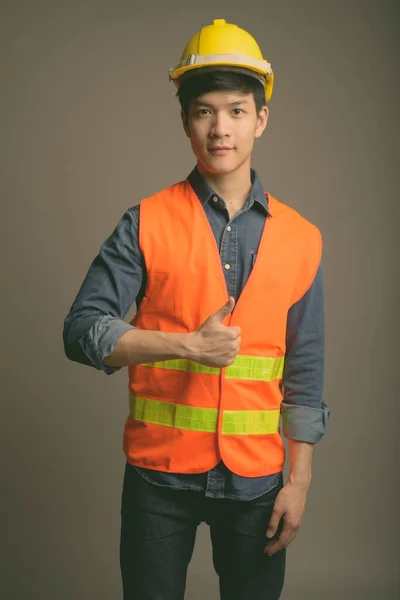 Genç yakışıklı Asyalı inşaat işçisi gri arka planda — Stok fotoğraf