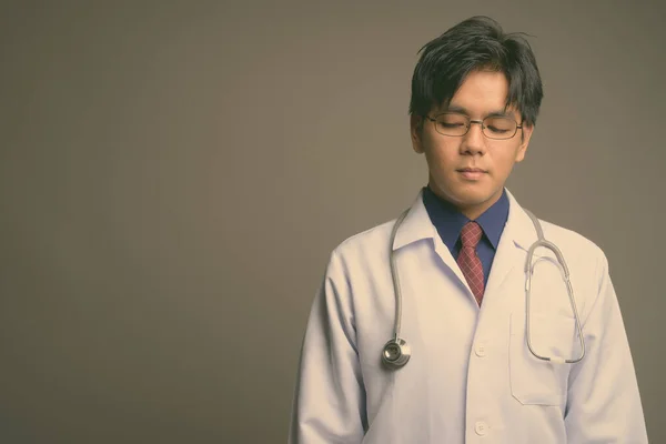 Young handsome Asian man doctor wearing eyeglasses against gray background — Stock Photo, Image