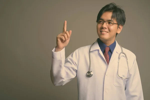 Joven guapo asiático hombre médico usando anteojos contra gris fondo —  Fotos de Stock