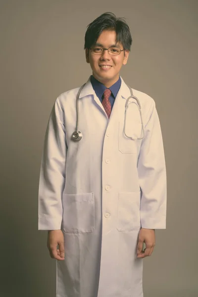 Joven guapo asiático hombre médico usando anteojos contra gris fondo — Foto de Stock