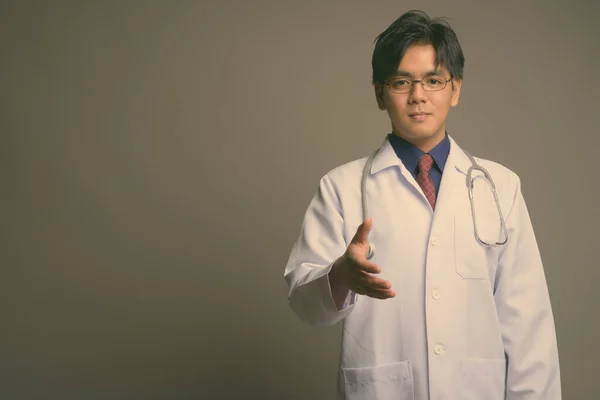 Joven guapo asiático hombre médico usando anteojos contra gris fondo —  Fotos de Stock