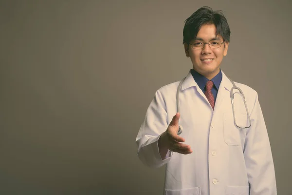Joven guapo asiático hombre médico usando anteojos contra gris fondo —  Fotos de Stock
