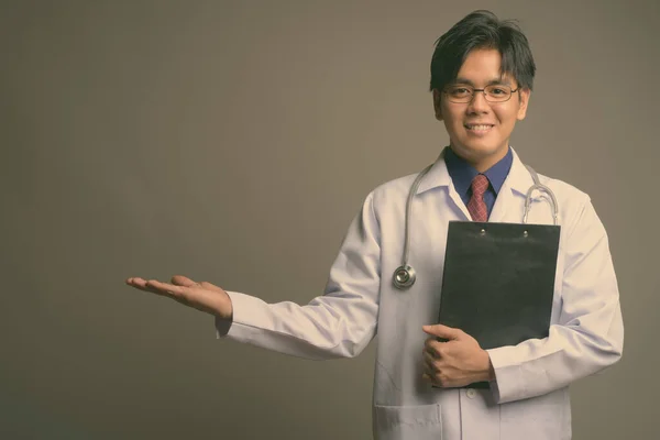Jeune beau asiatique homme médecin portant des lunettes sur fond gris — Photo