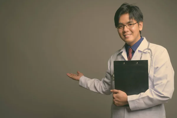 Молодий привабливий азіатський лікар з окулярами на сірому фоні. — стокове фото