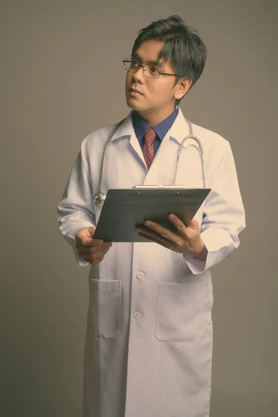 Jovem bonito ásia homem médico vestindo óculos contra cinza fundo — Fotografia de Stock