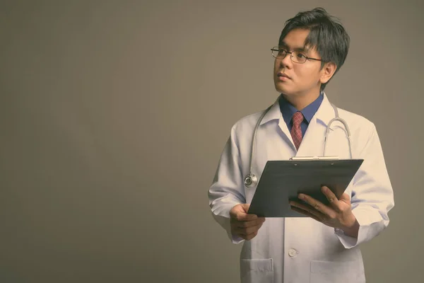 年轻英俊的亚洲男子医生，戴着灰色背景的眼镜 — 图库照片