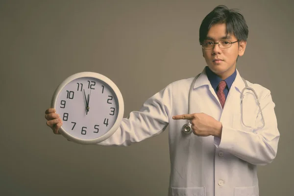 Fiatal jóképű ázsiai férfi orvos visel szemüveg ellen szürke háttér — Stock Fotó