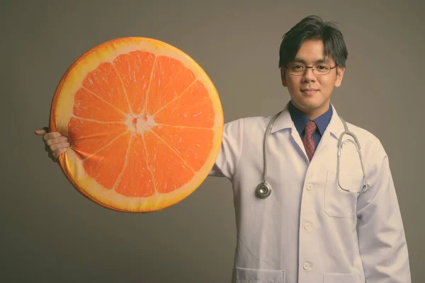 Młody przystojny Azji mężczyzna lekarz noszenie okulary na szare tło — Zdjęcie stockowe