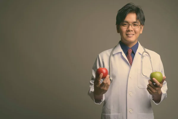 Genç yakışıklı Asyalı doktor, gri arka planda gözlük takıyor. — Stok fotoğraf