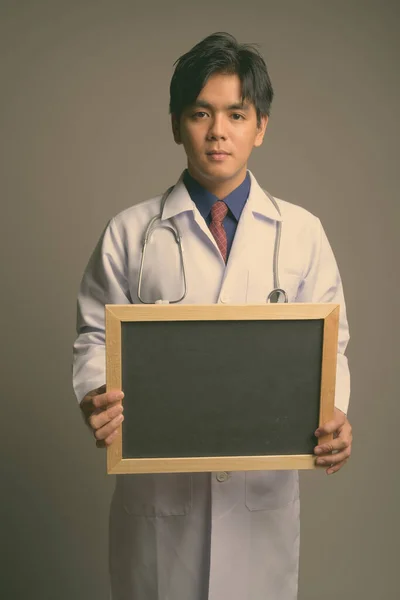 Young handsome Asian man doctor against gray background — Stock Photo, Image