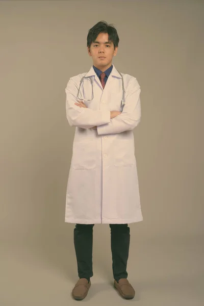 Молодой красивый азиатский врач на сером фоне — стоковое фото
